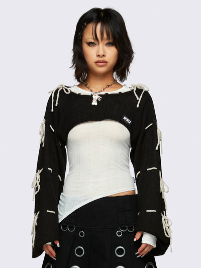 Black knitted shrug with white tie bows, designed in a bolero style with long, wide sleeves.