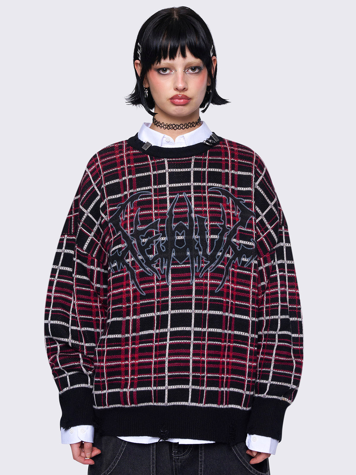 Plaid knitted jumper in red and black with a bold graphic print on the front. Features distressed rib details and a black ribbed neckline accented with piercing detail.