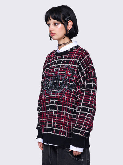 Plaid knitted jumper in red and black with a bold graphic print on the front. Features distressed rib details and a black ribbed neckline accented with piercing detail.