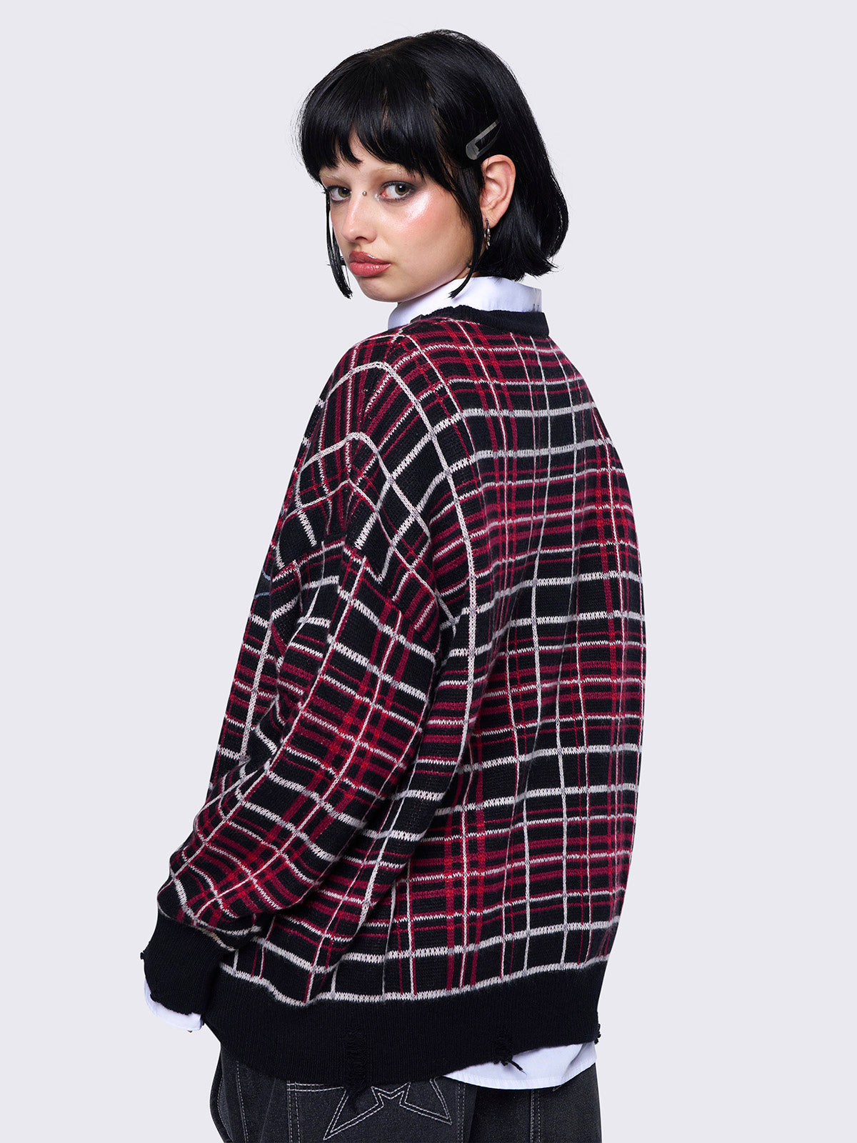 Plaid knitted jumper in red and black with a bold graphic print on the front. Features distressed rib details and a black ribbed neckline accented with piercing detail.