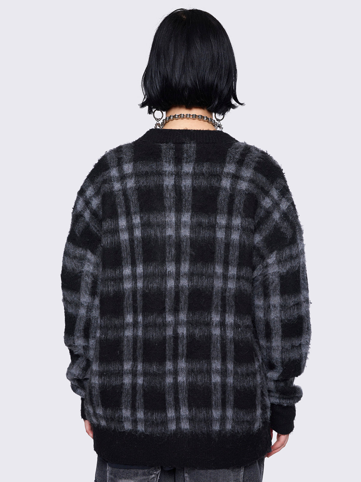 Black and grey plaid oversized cardigan, featuring a soft fuzzy texture and button-down front, paired with graphic t-shirt for an alternative fashion look.