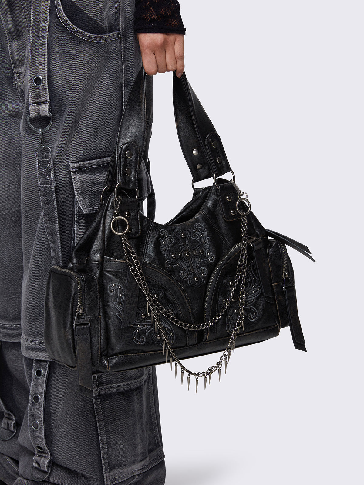 Washed black faux leather shoulder bag featuring studded cross patches, spike and chain accents, and multiple pockets.