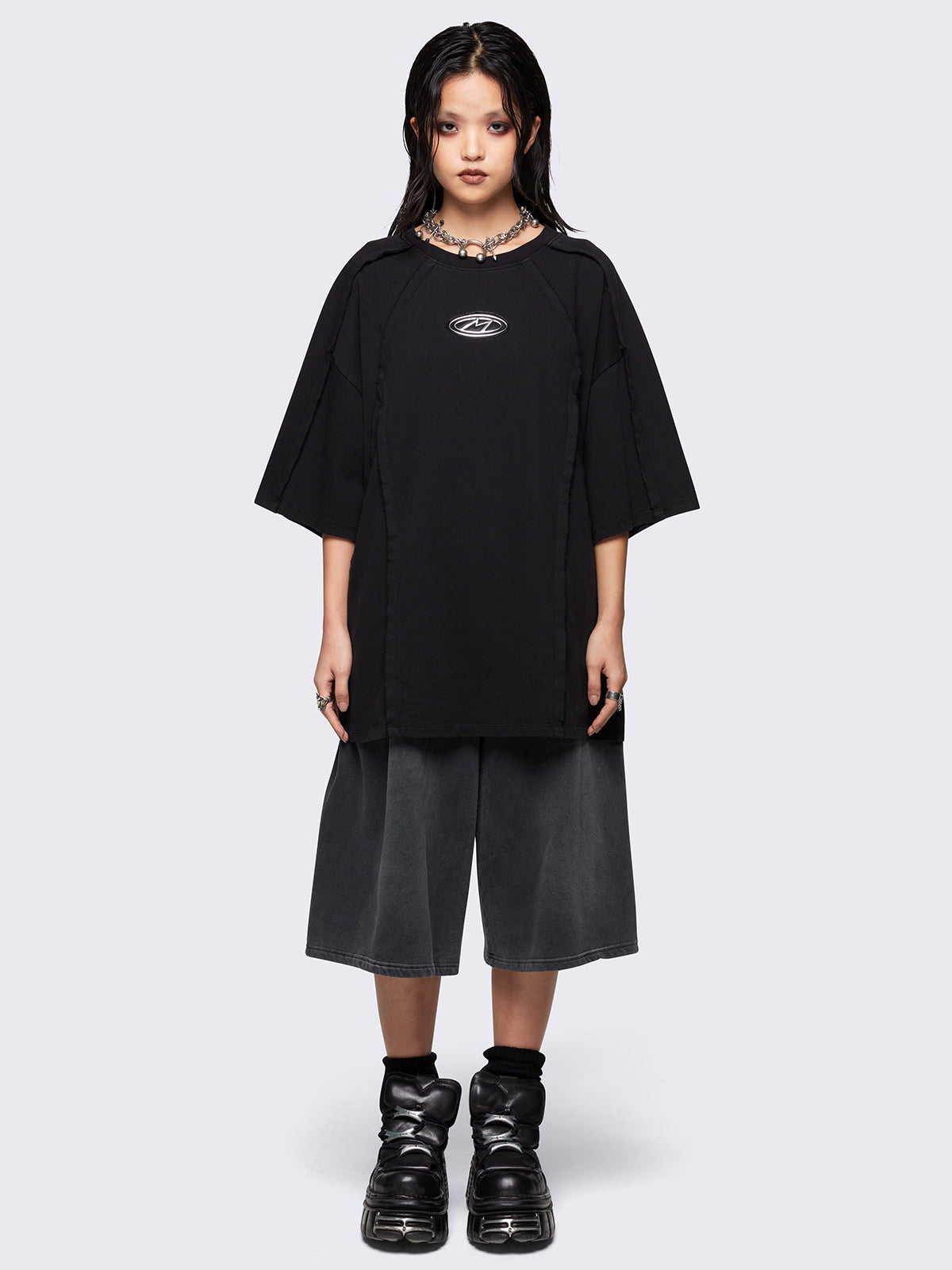 Black oversized t-shirt featuring exposed seams details and front metallic signature patch detail. 