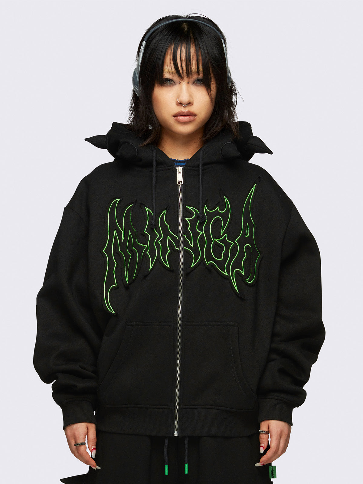 Black zip-up hoodie jacket featuring 3D spikes, green Minga embroidery, a drawstring hood, and zip fastening.