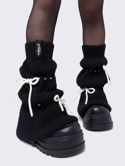 Black knitted leg warmers with white tie bows and a flared style.