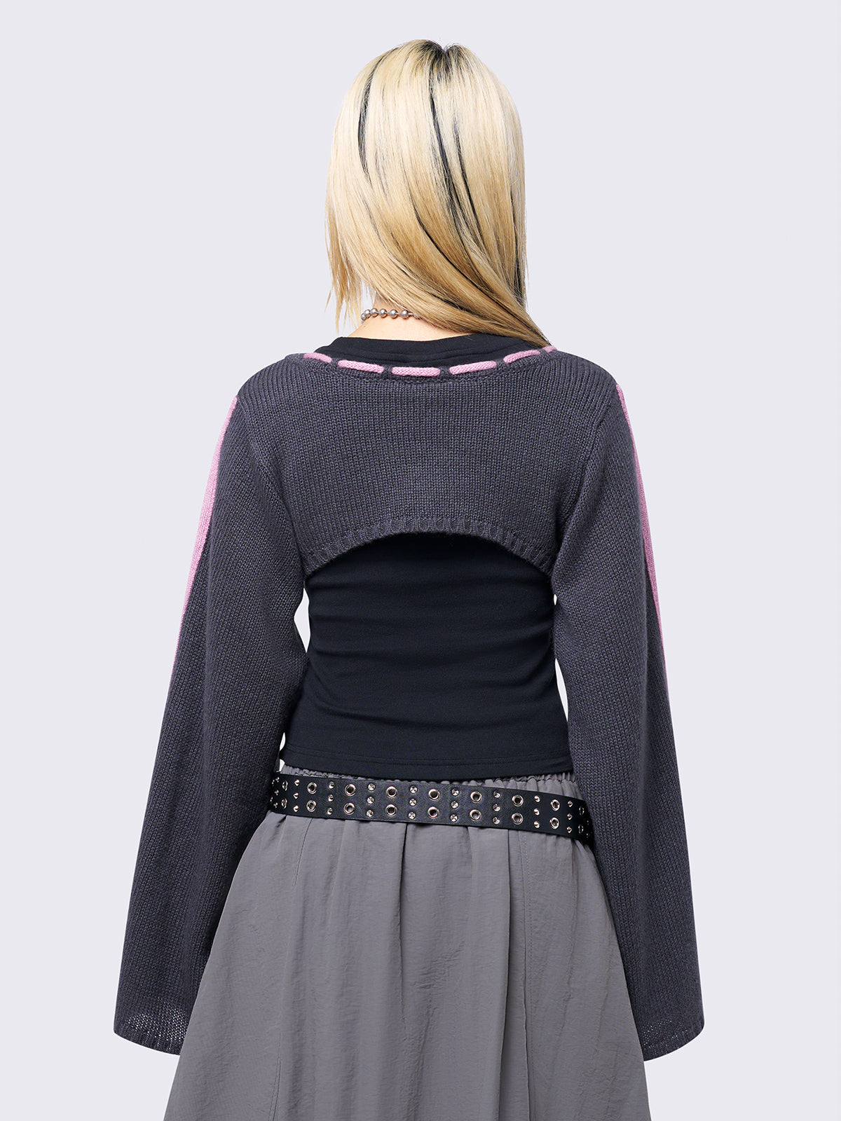 Grey knitted shrug with pink tie bow and striped details on the sleeves. Features a bolero style, long wide sleeves, and a super cropped length.